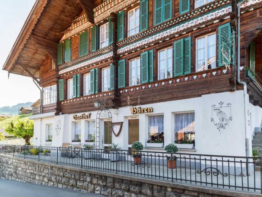 Un edificio tradicional de madera con contraventanas verdes, un letrero que dice "Bären" y un muro de piedra al frente.