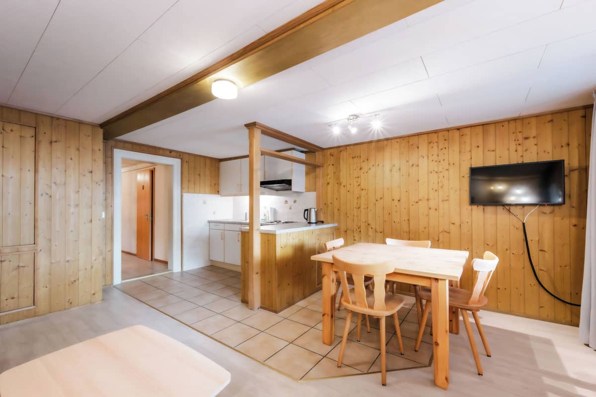 Une pièce aux murs lambrés, comprenant une cuisine, un coin repas et un téléviseur fixé au mur.