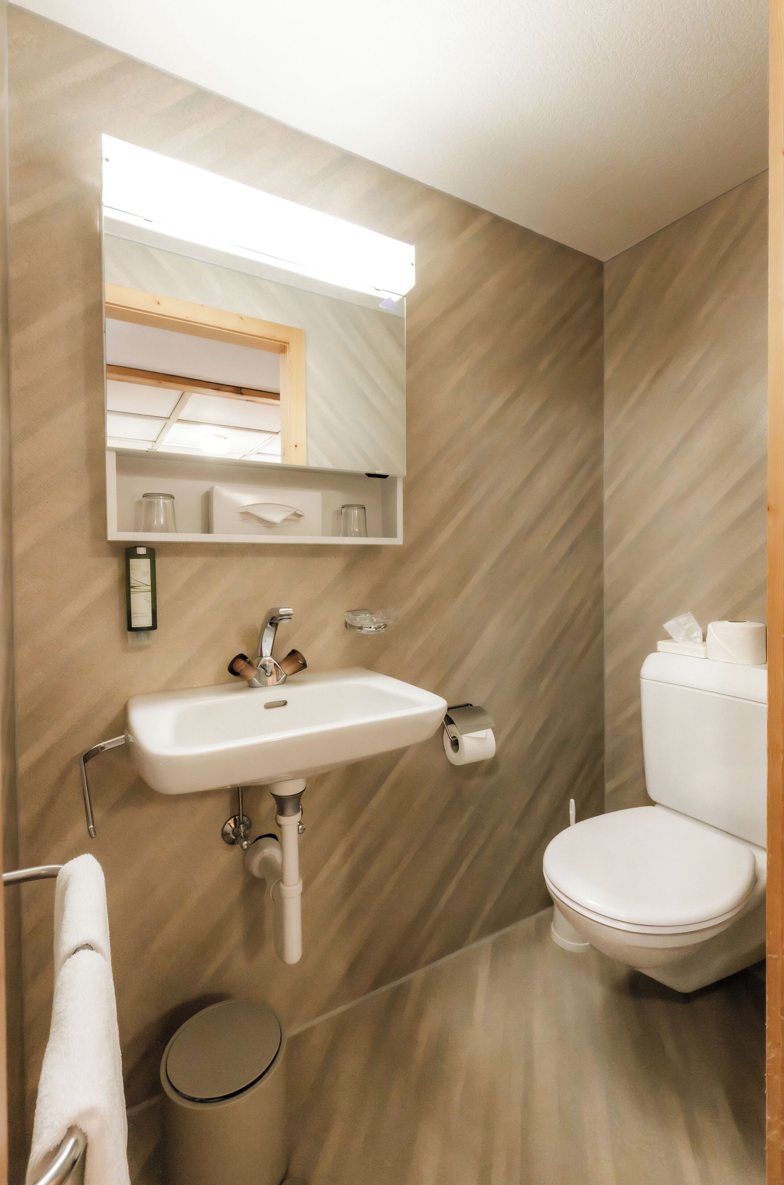 Un baño con lavamanos, espejo, inodoro y un cubo de basura.