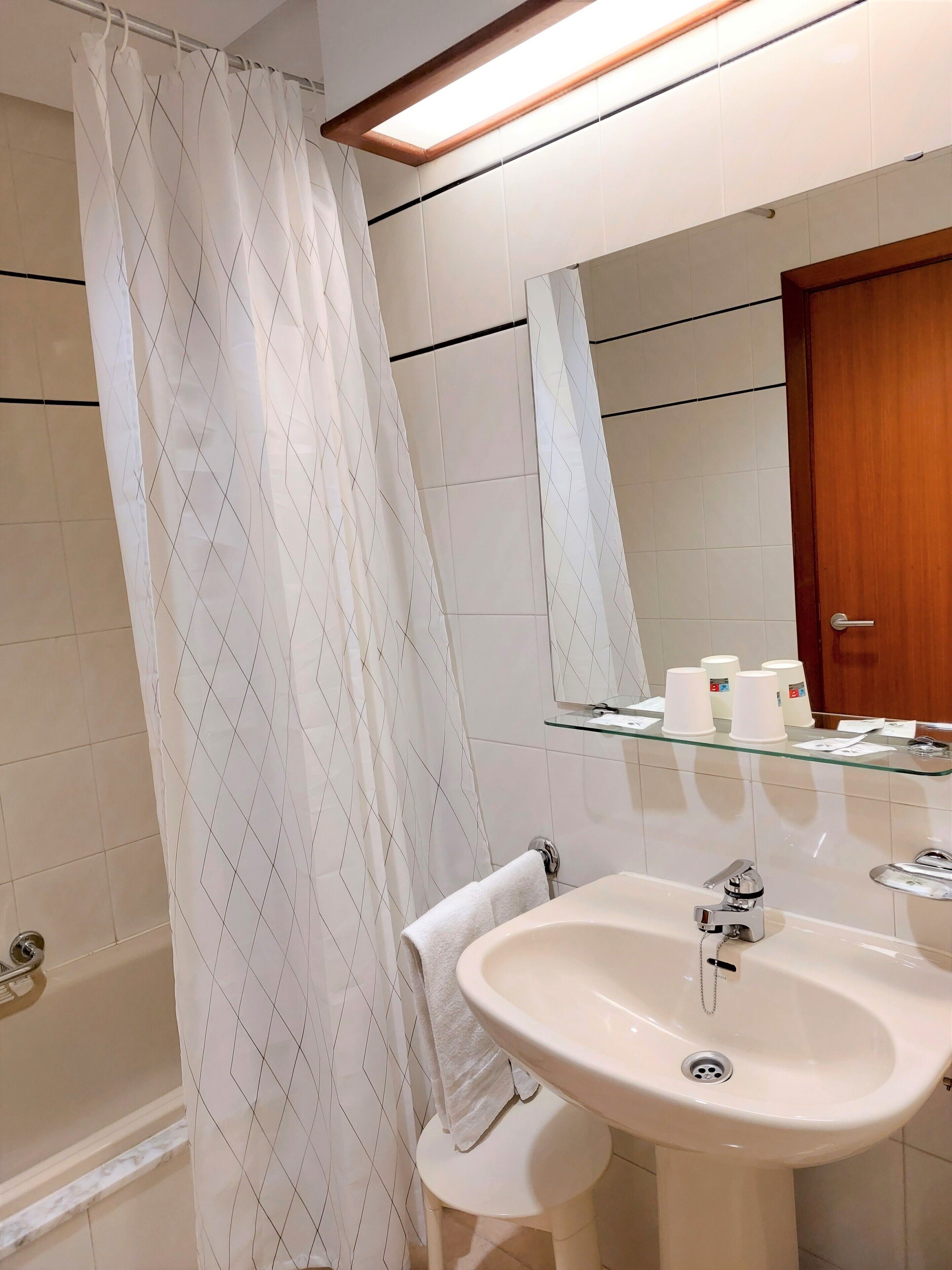 Une salle de bain avec un rideau de douche, un lavabo, un miroir et une étagère en verre où sont rangés les articles de toilette.
