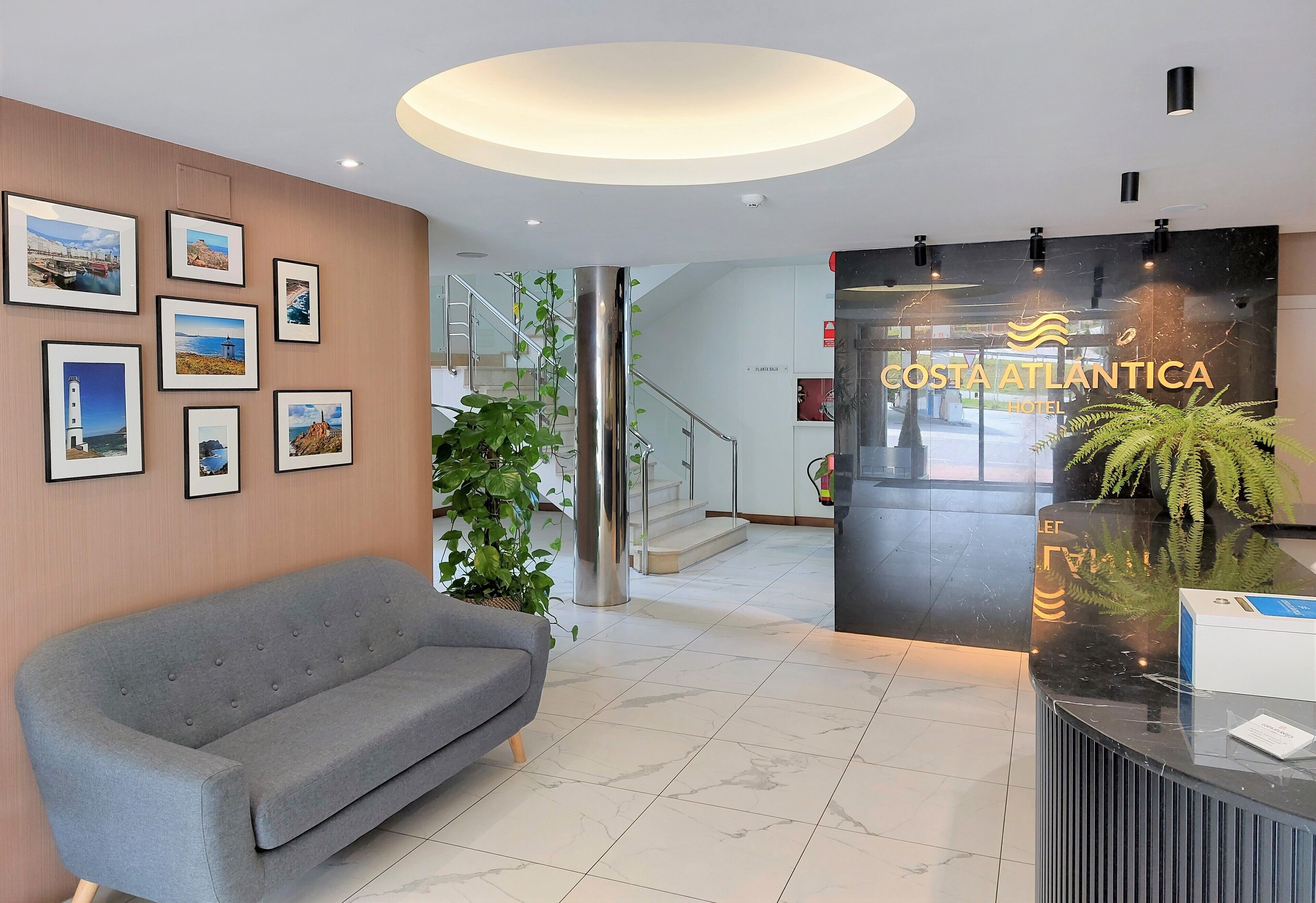 Ein Hotel-Rezeptionsbereich mit einer grauen Couch, gerahmten Bildern an der Wand und einem Empfangstresen mit Pflanze.