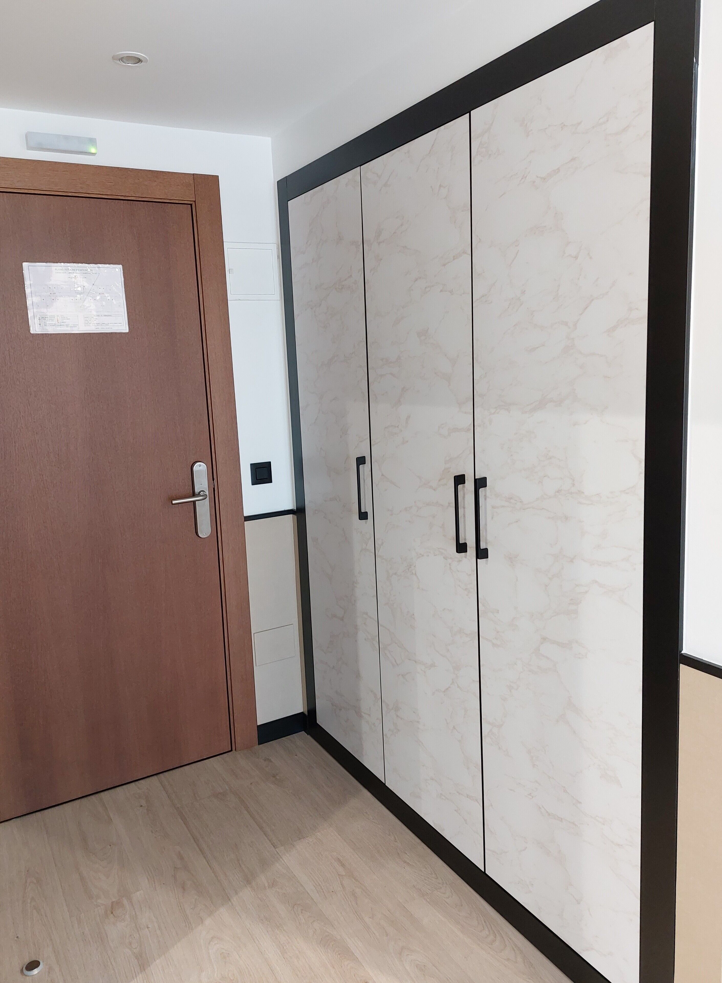 A room with a wooden door, a wardrobe with a marble finish, and a light-colored wooden floor.
