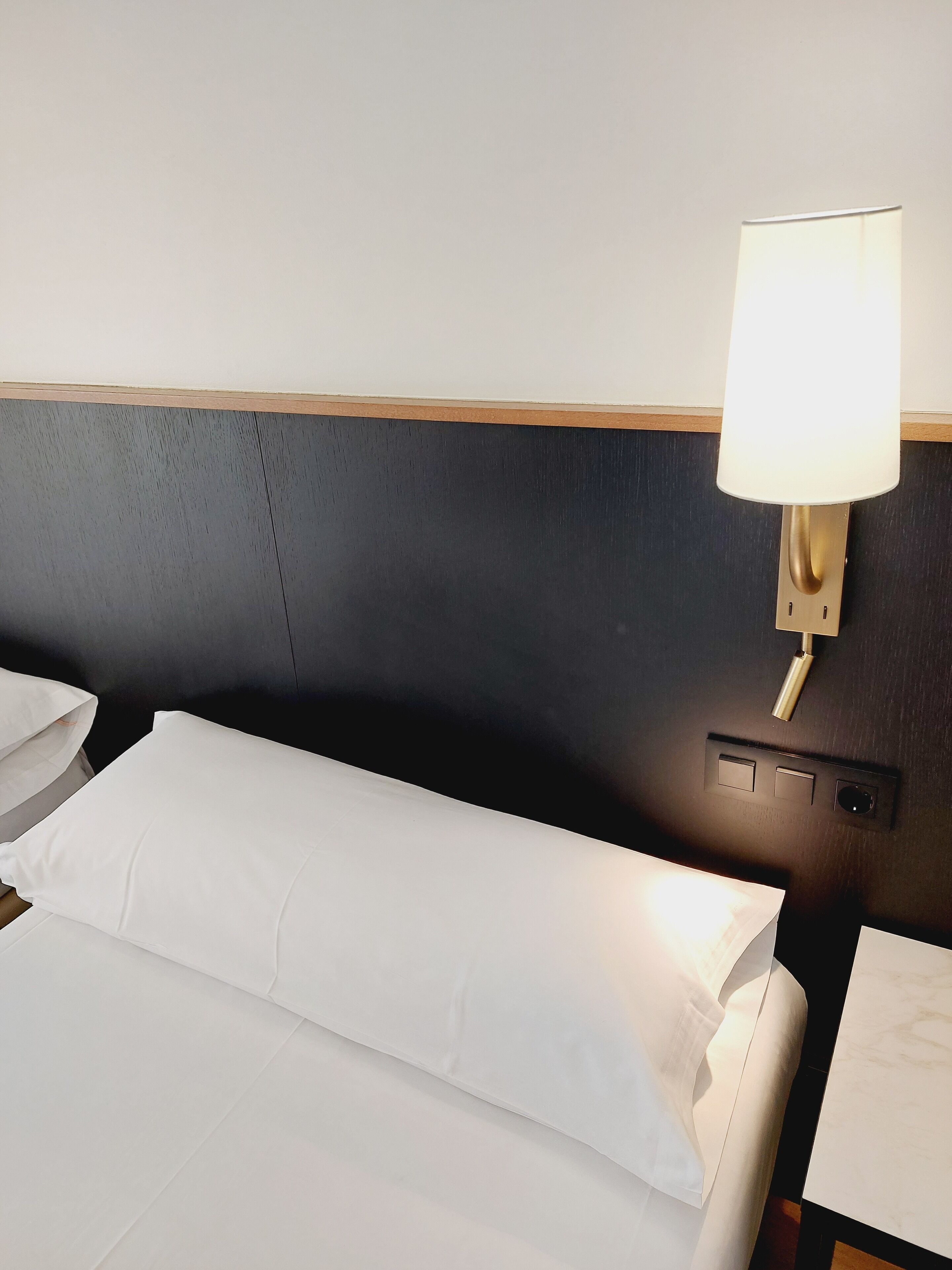 Une chambre d’hôtel équipée d’un lit, d’une lampe fixée au mur et d’un panneau de commande.