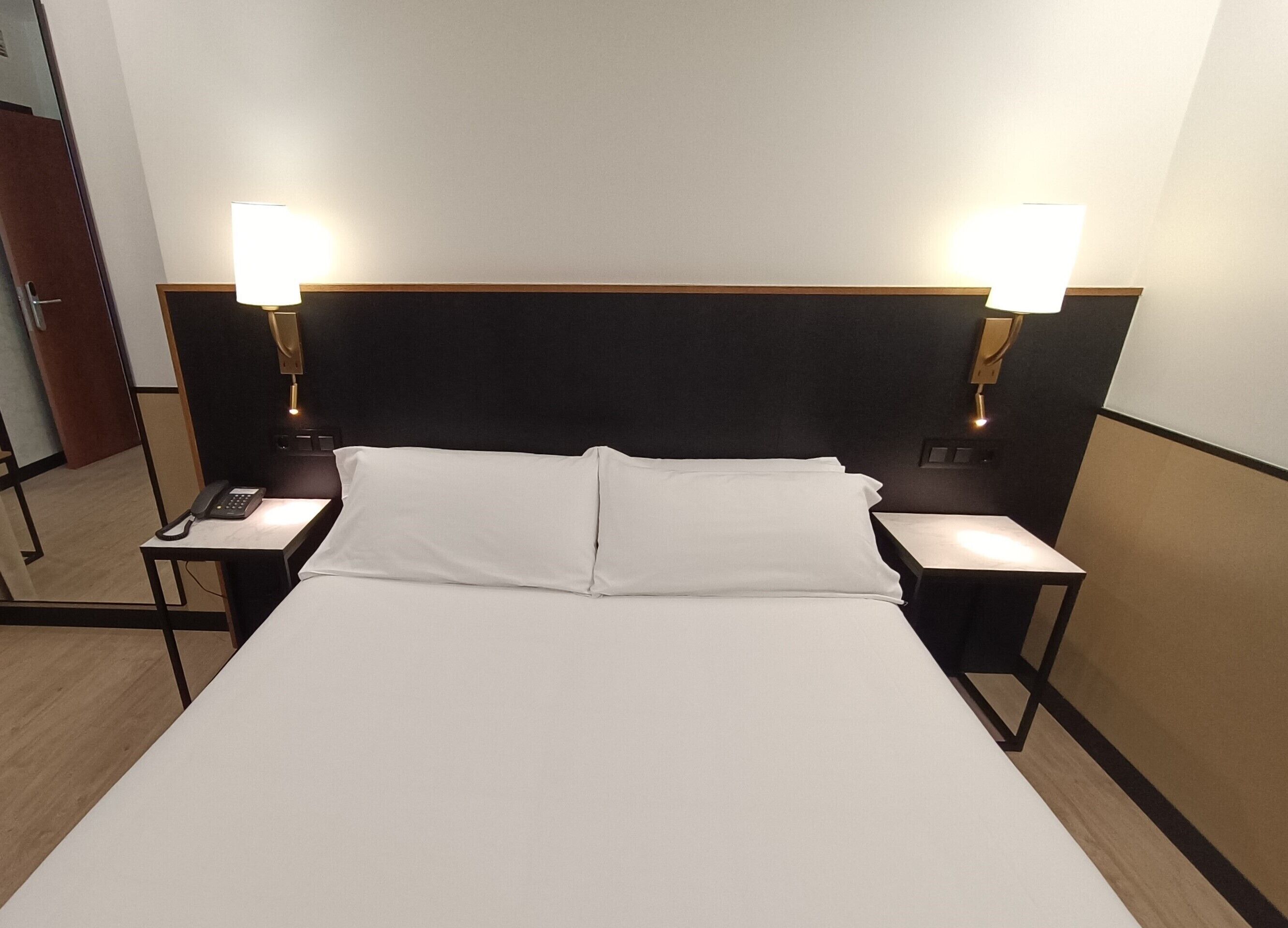 Habitación de hotel con una cama grande, dos mesitas de noche con lámparas y un cabecero de madera.