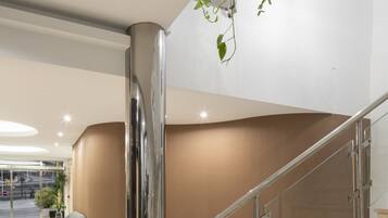Un vestíbulo moderno con piso de mármol, un mostrador de recepción curvo, una gran columna metálica y una escalera con barandillas de vidrio.