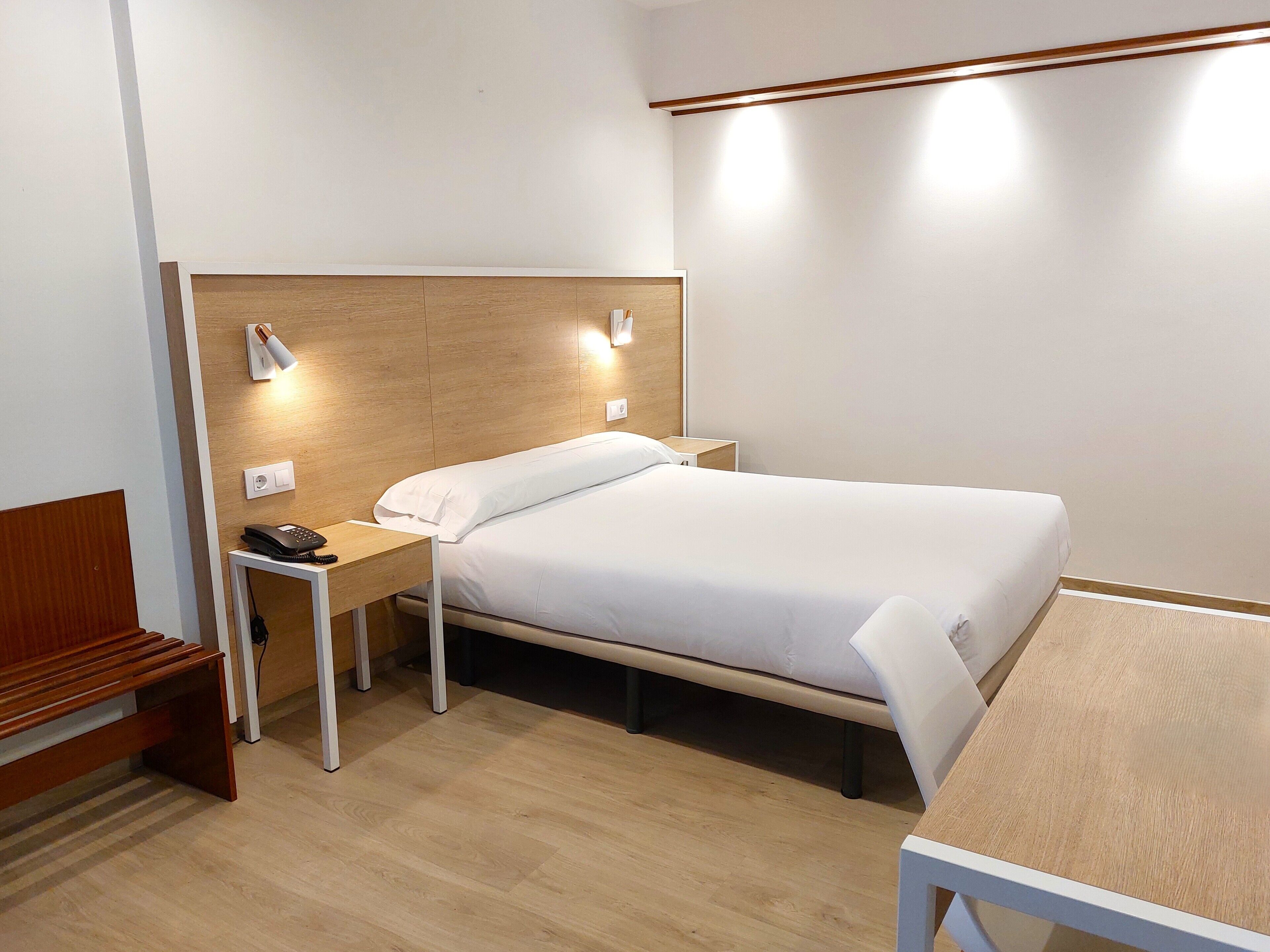 Una habitación de hotel ordenada con una cama individual, una mesita de noche y un escritorio pequeño con una silla.