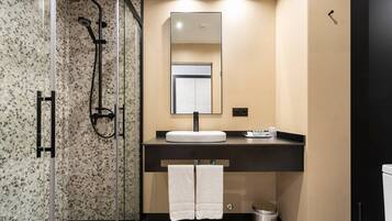 Un baño moderno con ducha envuelta en vidrio, tocador con lavamanos y espejo superior.