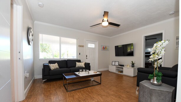 A modern living room with a black sofa, a coffee table, a TV, and a ceiling fan. - 4BR Home, Hot Tub, Near Beach & Wilton Manors (Oakland Park)