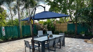 An outdoor patio with a table and chairs, a blue umbrella, and a 'LOVE' sign. - 4BR Home, Hot Tub, Near Beach & Wilton Manors (Oakland Park)
