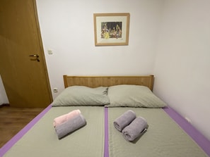 Quarto com uma cama, duas toalhas enroladas, uma porta e um quadro na parede.