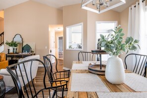 Un coin repas avec une table en bois, des chaises noires et un vase blanc contenant des plantes vertes.
