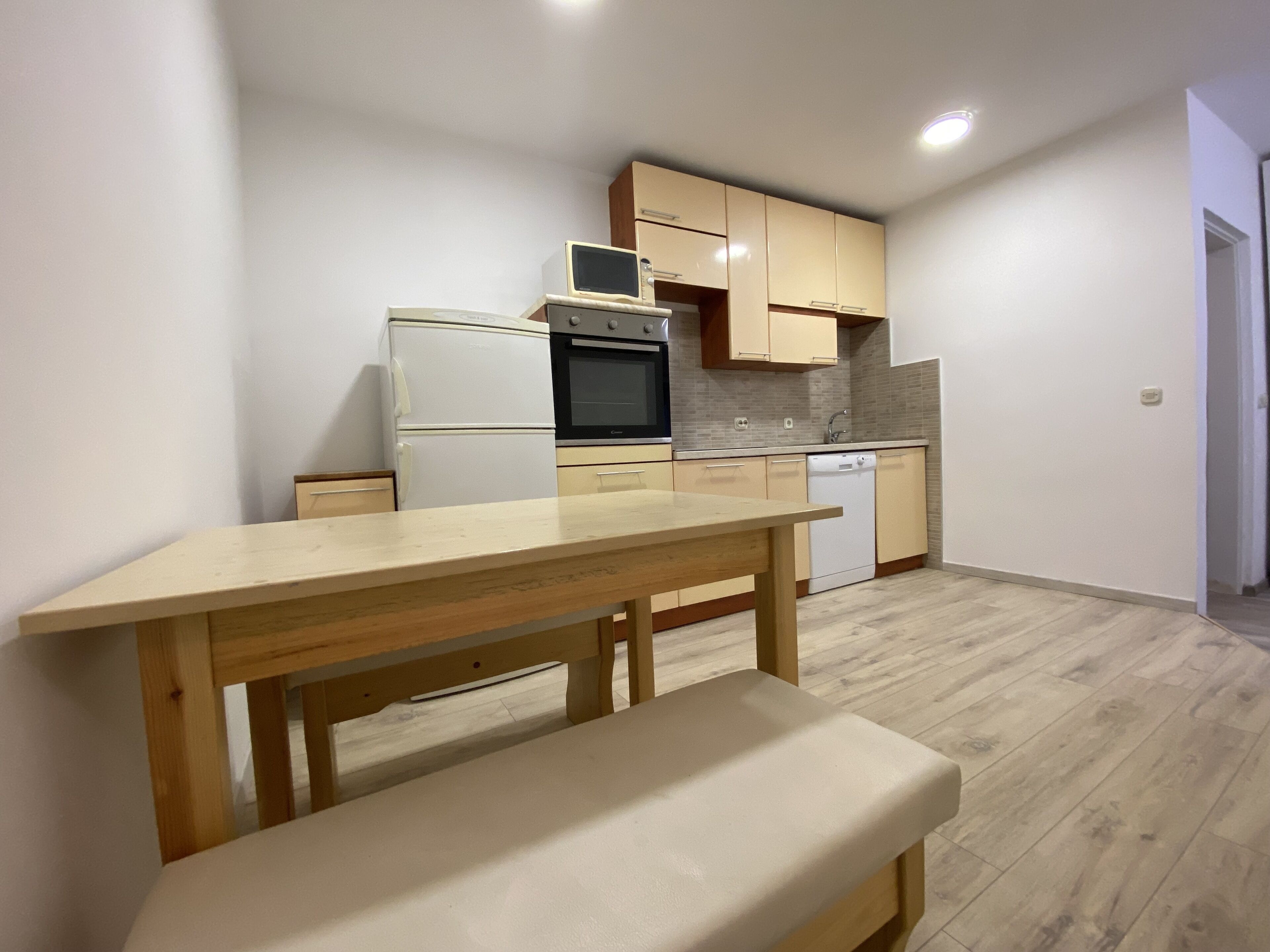 A compact kitchen with a wooden table and bench, a refrigerator, oven, microwave, and dishwasher.