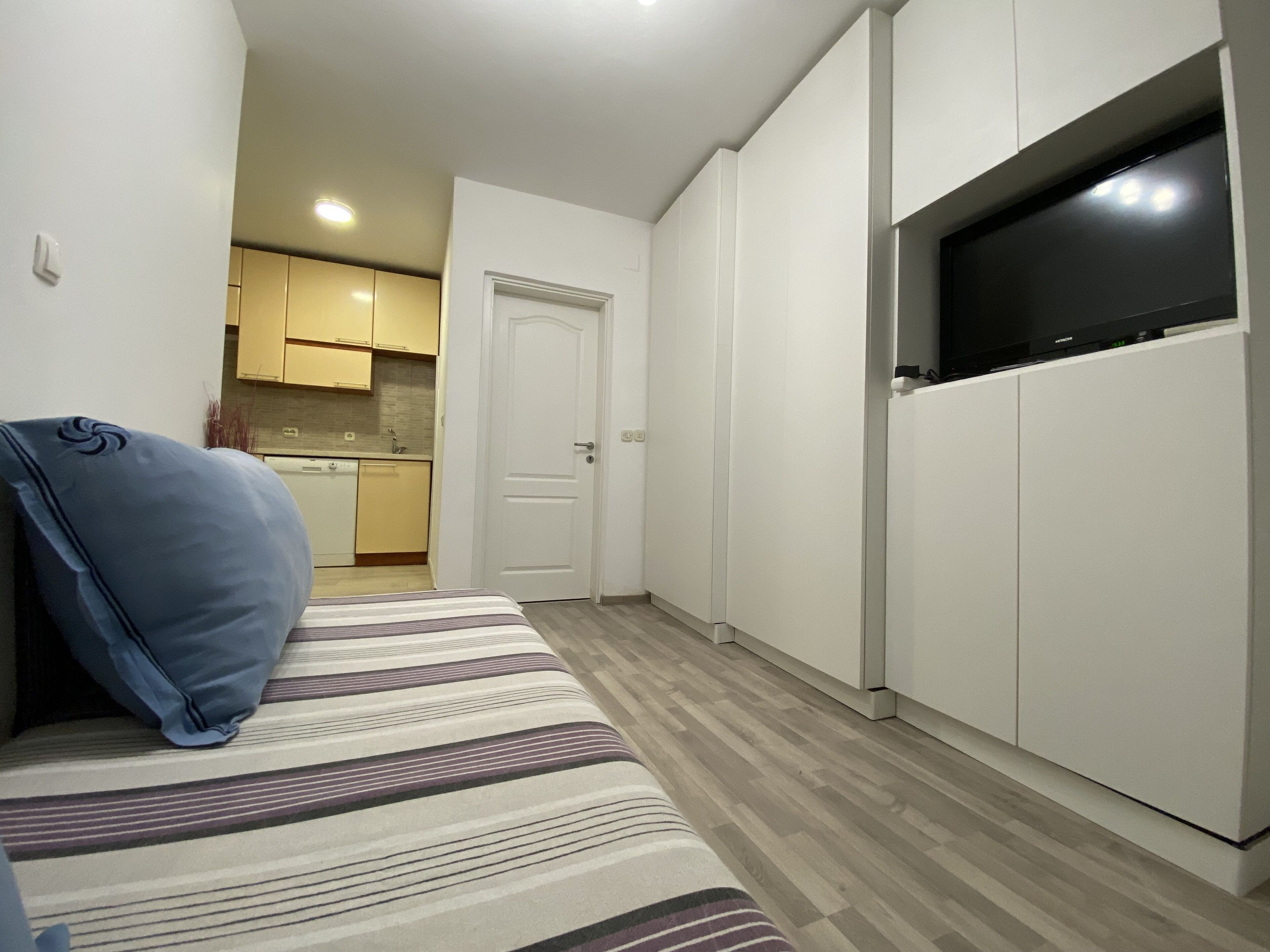 En kompakt opholdsstue med sofa, fjernsyn og et tekøkken i baggrunden.