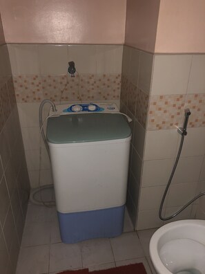 A compact bathroom with a toilet, a washing machine, and a shower.
