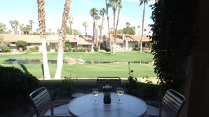 Eine Terrasse mit einem runden Tisch und vier Stühlen, mit Blick auf einen gepflegten Rasen und einen Golfplatz.
