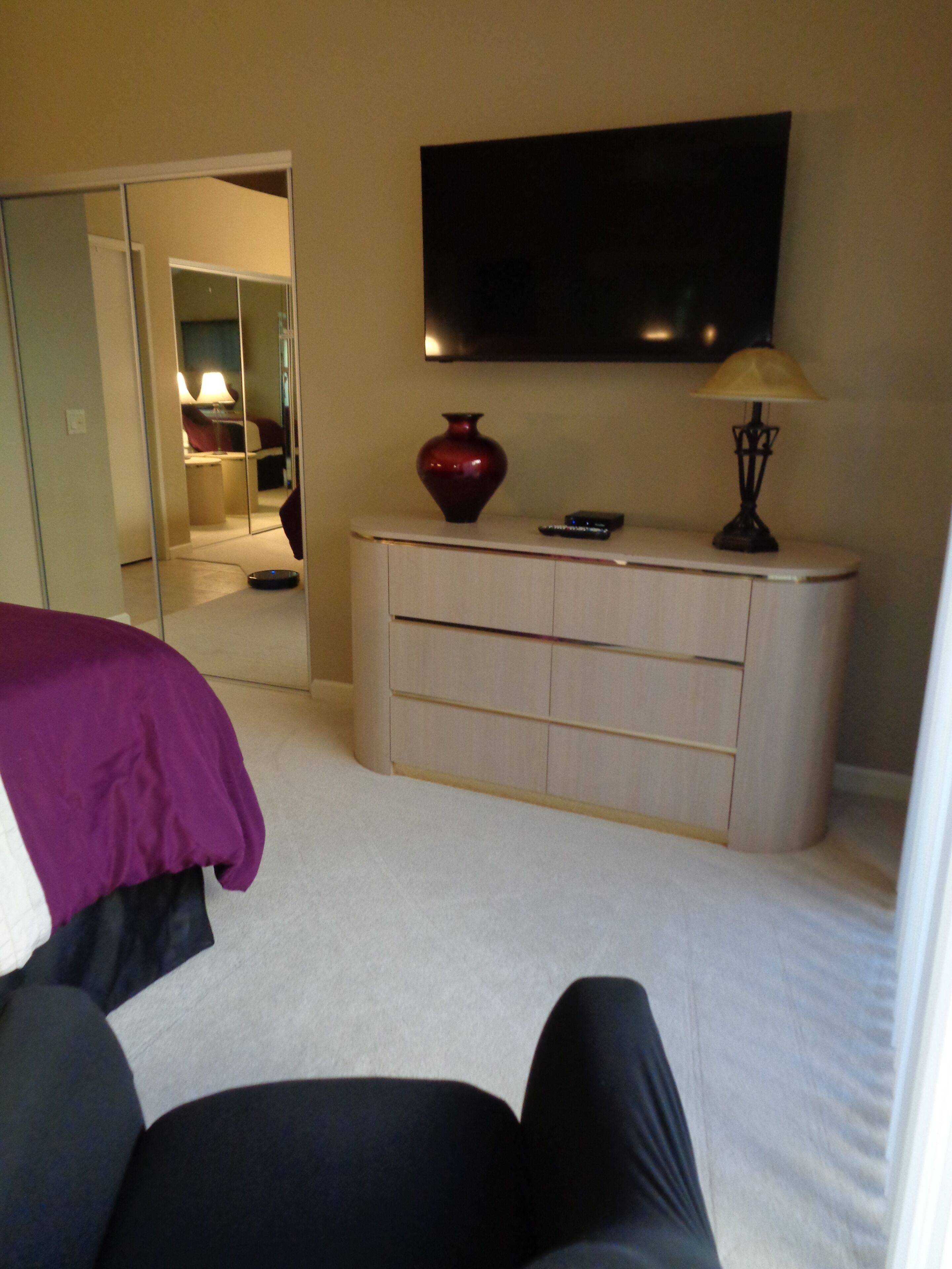 Een slaapkamer met een bed, een dressoir, een televisie en een spiegel.
