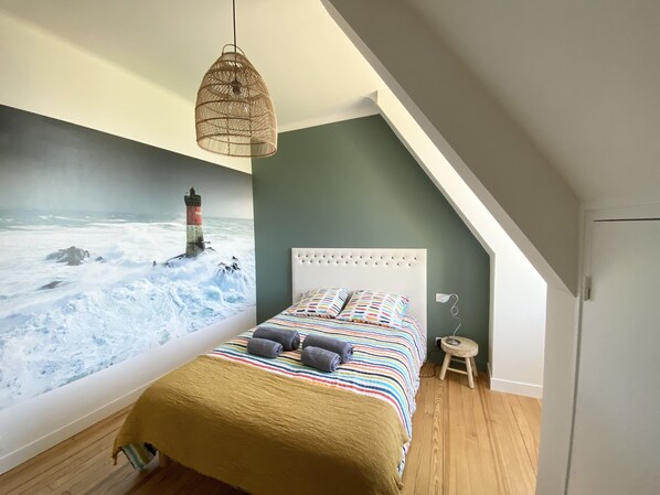 A bedroom with a mural of a lighthouse, a white tufted headboard, a striped bedspread, and a small wooden stool. - Grande Villa, vue Mer, à Bénodet (Bénodet)
