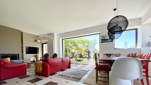A modern living room with a red sofa, a dining table with red chairs, and a large window with a view of greenery. - Grande Villa, vue Mer, à Bénodet (Bénodet)