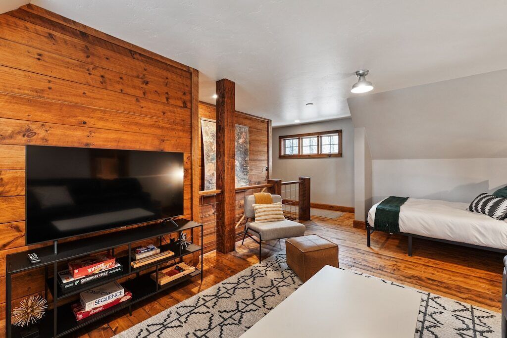 A cozy living room with a large flat-screen TV, wooden walls, a comfortable sofa, and a small table.