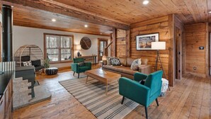 A spacious living room with wooden floors and walls, a sofa set, a coffee table, and a large window providing natural light.