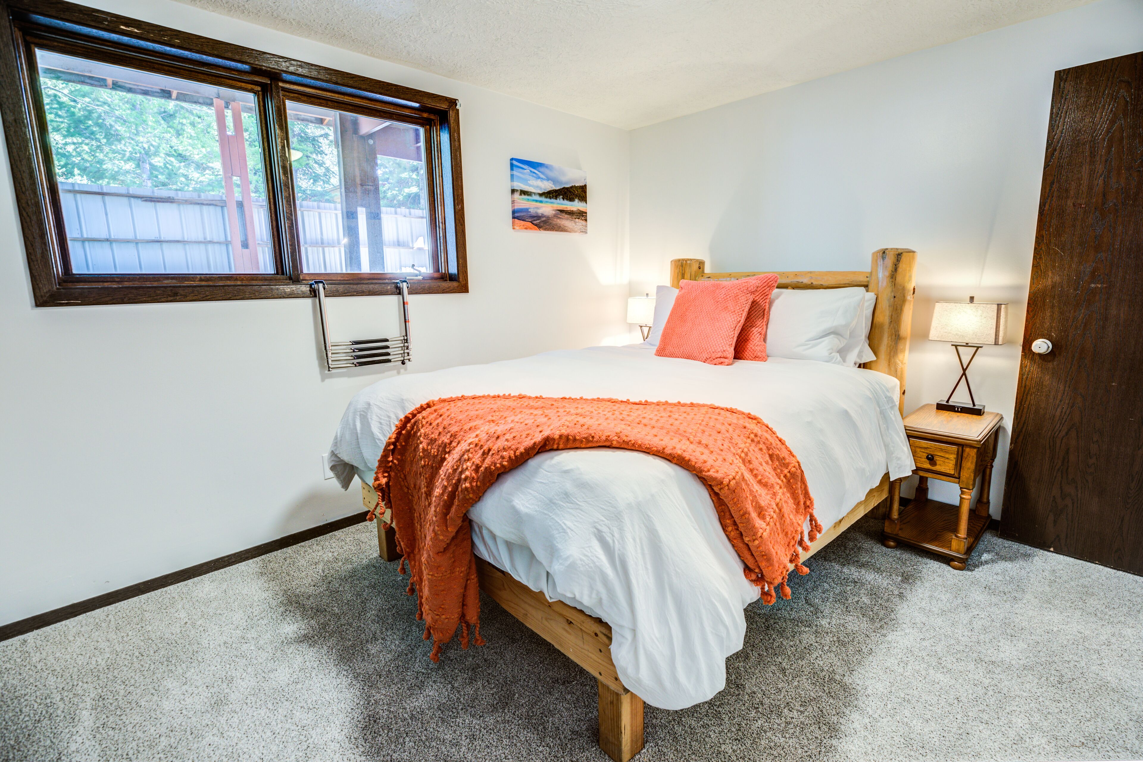 A bedroom with a bed, a window, a painting, and a nightstand.