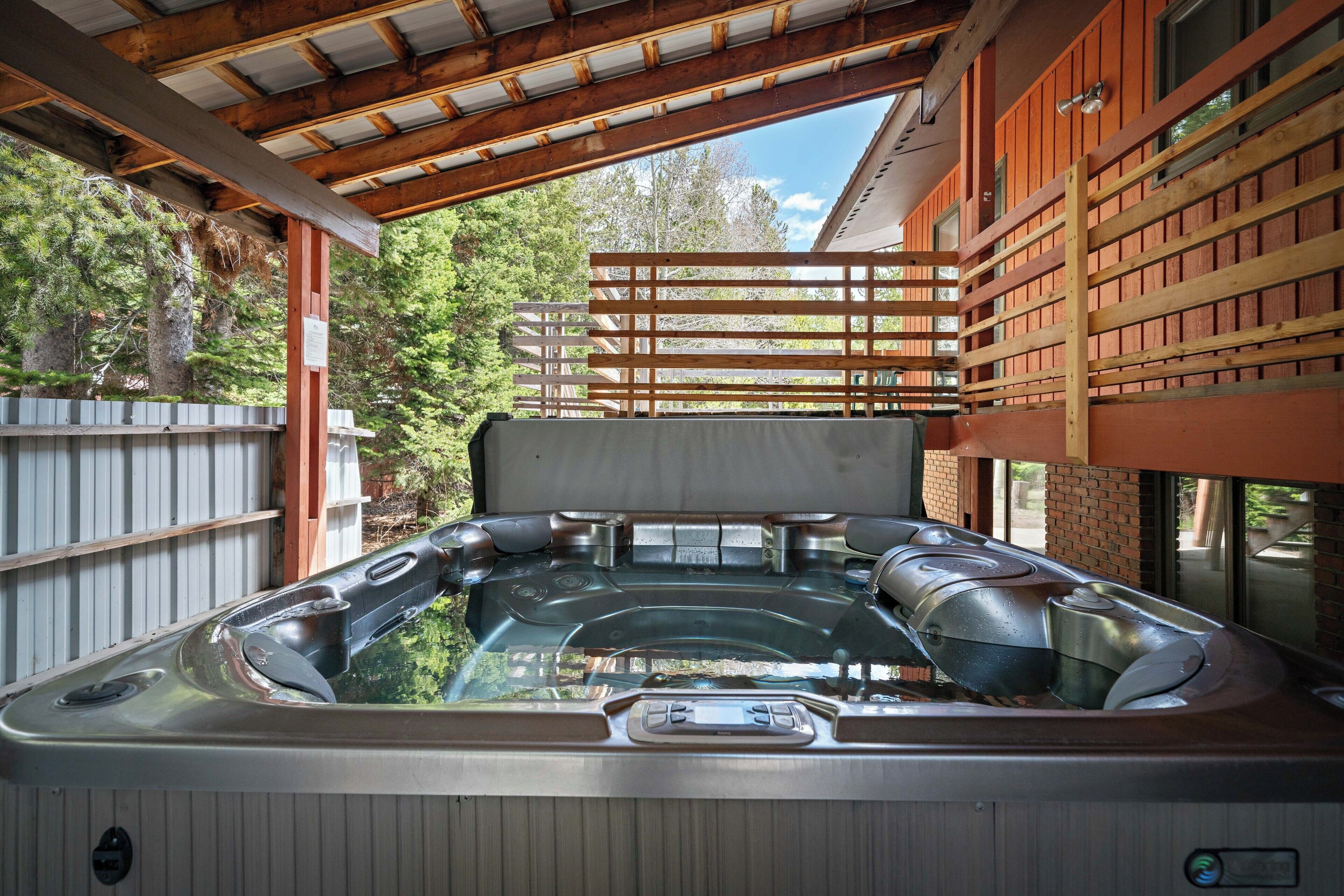 A hot tub under a wooden pergola with a view of trees.