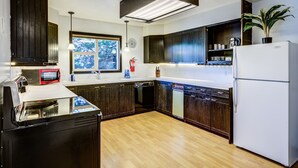 A modern kitchen with dark wooden cabinets, a white refrigerator, and a built-in dishwasher. - Geyser Getaway (West Yellowstone)