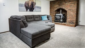A living room with a gray sectional sofa, a fireplace, and two framed pictures on the wall. - Geyser Getaway (West Yellowstone)