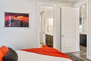 Une chambre à coucher avec un lit, une couverture rouge, un tableau, et une salle de bain visible à travers une porte ouverte.