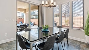 Een moderne eethoek met een glazen tafel, zwarte stoelen en een kroonluchter.