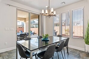 Een moderne eethoek met een glazen tafel, zwarte stoelen en een kroonluchter.