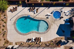 An aerial view of a swimming pool with lounge chairs and a hot tub area.