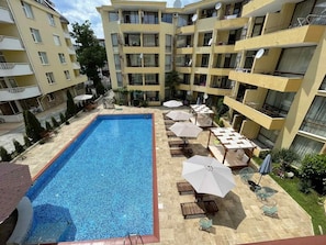 A multi-story residential building with a central swimming pool surrounded by lounge chairs and umbrellas. - Stylish 1-bed Apartment in Sunny Beach (Sunny Beach)