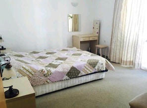 A bedroom with a bed, a desk, a chair, a mirror, and a window with curtains.