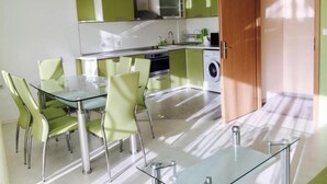 A modern kitchen with green cabinets, a glass dining table, and a washing machine. - Stylish 1-bed Apartment in Sunny Beach (Sunny Beach)