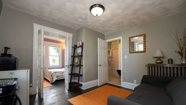 A living room with a sofa, a coffee table, a bookshelf, and a door leading to another room. - 1 Bedroom Studio and 1 Full Bathroom-Close to Beach, Encore and TD Garden Arena. (Chelsea)