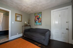 Ein Zimmer mit grauem Sofa, einer weißen Tür, einem gerahmten Poster und einer Heizung.