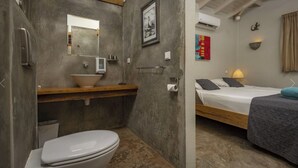 A compact bathroom with a toilet, sink, and mirror. Adjacent is a bedroom with a bed, bedside lamp, and a wall-mounted air conditioner. - your favorite hangout on Bonaire (Kralendijk)