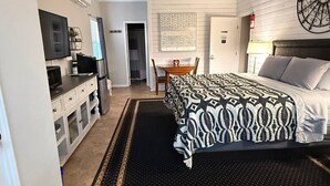 Ein Hotelzimmer mit Bett, Schreibtisch, Stuhl, Deckenventilator und einem an der Wand befestigten Fernseher.