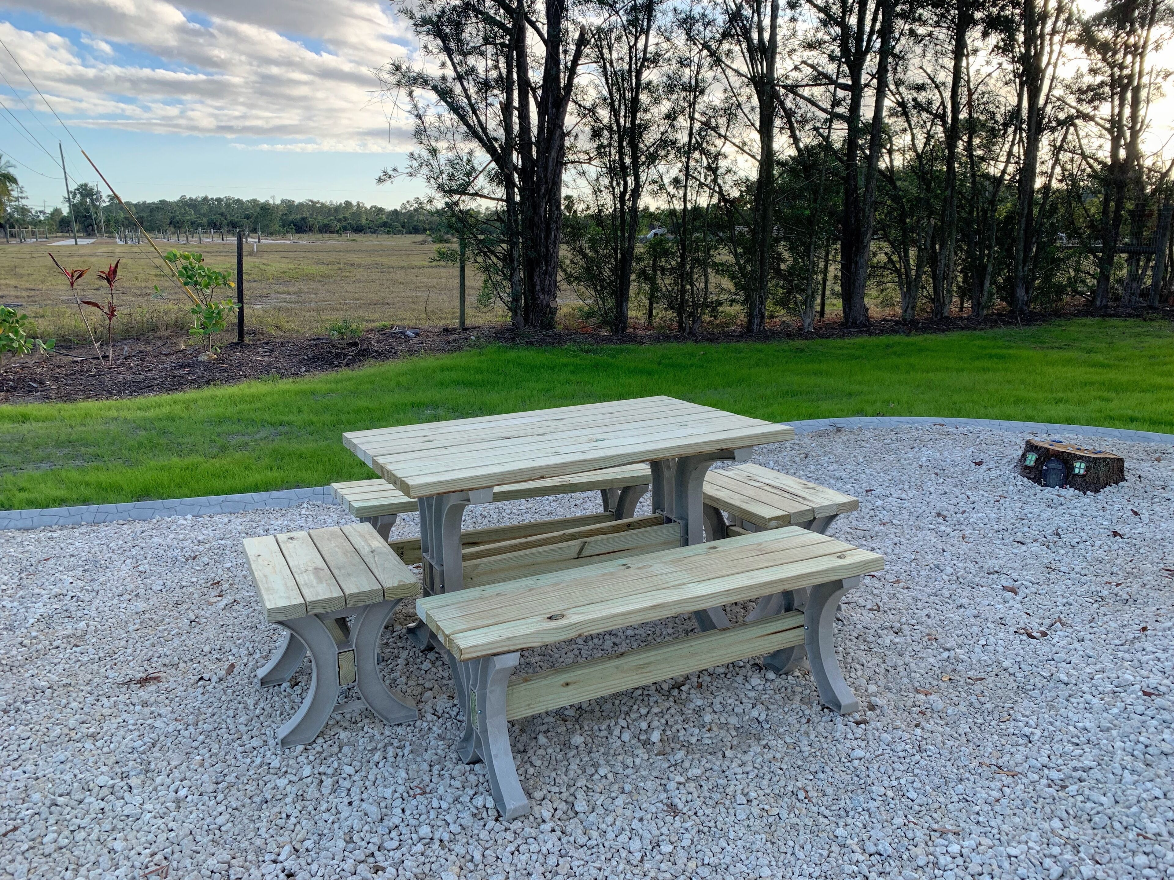 A picnic table with benches in a gravel area surrounded by trees.