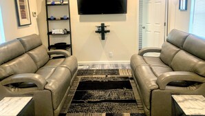 Un salon avec deux canapés en cuir, un téléviseur à écran plat, une bibliothèque et un tapis à motifs.