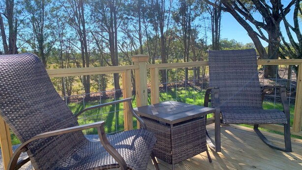 Une terrasse en bois, dotée de meubles en osier et d’une table, qui offre une vue sur une zone boisée.