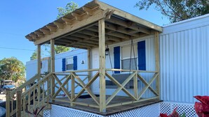 Une terrasse en bois avec une balustrade, une clôture blanche et un petit espace porche.