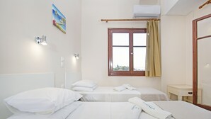 A hotel room with two beds, a window with curtains, a bedside table, and a wall-mounted air conditioner. - NIKOLOUZOS SUNNY ESTATE (Corfu)