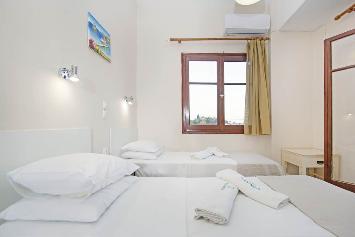 Ein Hotelzimmer mit zwei Betten, einem Fenster mit Vorhängen, einem Nachttisch und einer Wandklimaanlage.