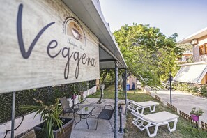 An outdoor seating area with tables and chairs, a pergola with a sign, and a view of a hillside.