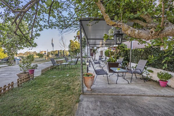 An outdoor patio area with tables and chairs, surrounded by potted plants and a tree.
