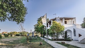 A white building with a stone pathway, outdoor seating, and a flag. - NIKOLOUZOS SUNNY ESTATE (Corfu)
