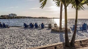 Una spiaggia con sedie e palme, un corpo d'acqua e edifici sullo sfondo.
