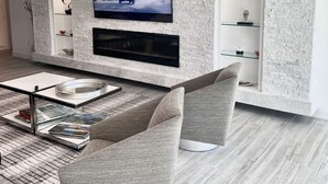 Un soggiorno moderno con una televisione a schermo piatto montata su una parete strutturata, un caminetto sottostante e un'accogliente area salotto con un tavolino.